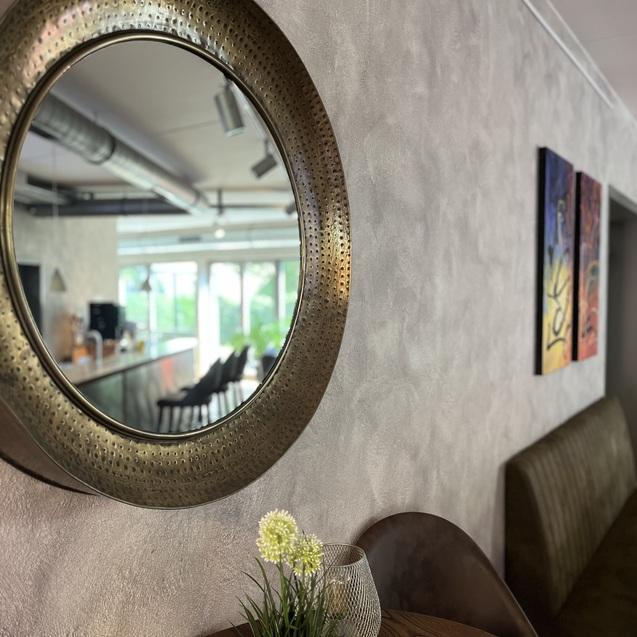 Runder Spiegel an einer Wand in einem modernen Café mit stylischen Sitzgelegenheiten und bunten Kunstwerken.