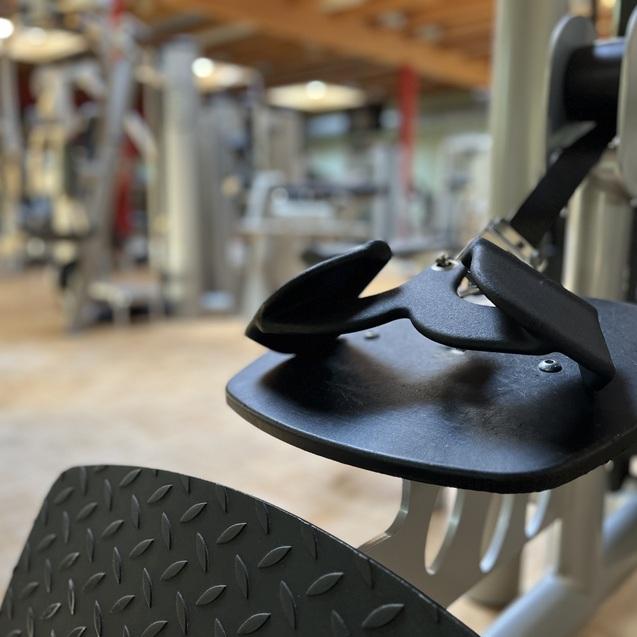 Nahaufnahme eines Fitnessgeräts mit Fußplatte und verstellbarem Riemen in einem modernen Trainingsstudio.