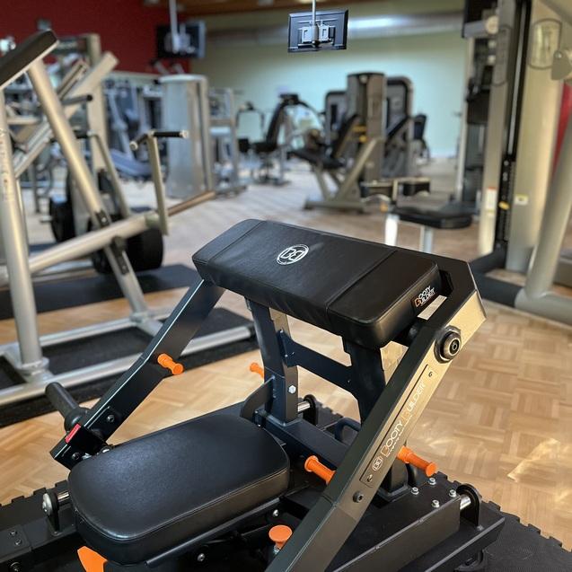 Nahaufnahme einer verstellbaren Fitnessbank mit Gewichten im Hintergrund in einem modernen Fitnessstudio.