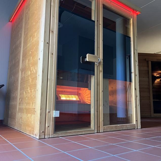 Holzsauna mit Glasfront und LED-Beleuchtung in einem sauberen Raum mit gefliester Terrasse.