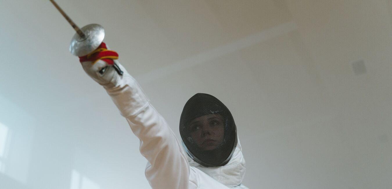 Fencers mit Maske und G&uuml;rtel hebt das Florett in einer sportlichen Haltung in einem nebeligen Umfeld.