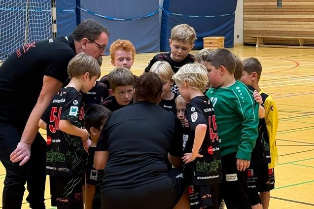 Gruppe von Kindern in Sportkleidung huddelt sich um Trainer in einer Sporthalle.
