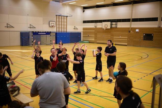 Gruppenspielende Kinder in Sportkleidung jubeln in einer Turnhalle nach einem erfolgreichen Spiel.