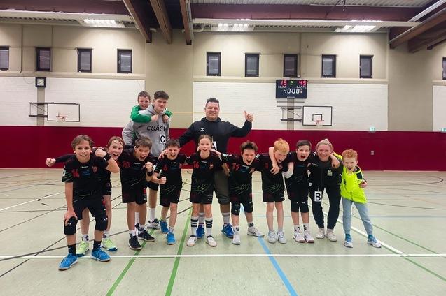 Gruppe von Kindern in Sportkleidung mit Trainer in einer Sporthalle, alle jubeln zusammen nach einem Spiel.