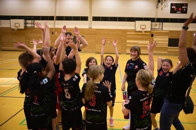 Gruppe von Kindern im Sportoutfit mit erhobenen H&auml;nden, jubelt in einer Sporthalle.