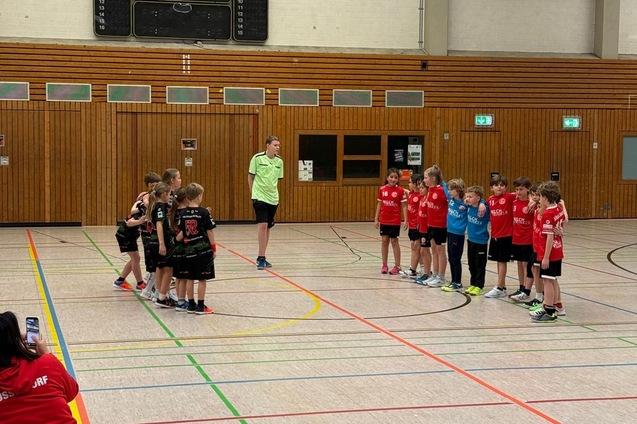 Gruppe von Kindern in Sportkleidung steht in zwei Reihen in einer Turnhalle, w&auml;hrend ein Trainer Anweisungen gibt.