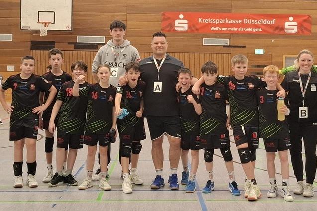 Gruppenfoto einer Jugend-Handballmannschaft mit Trainer, alle in schwarzen Trikots, in einer Sporthalle.