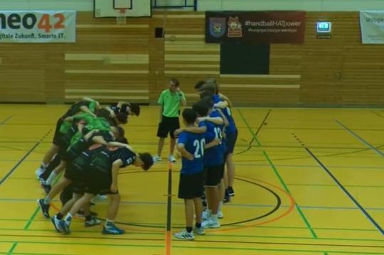 Gruppenbildung von Handballspielern in einer Sporthalle, stehen eng zusammen und besprechen die Taktik.