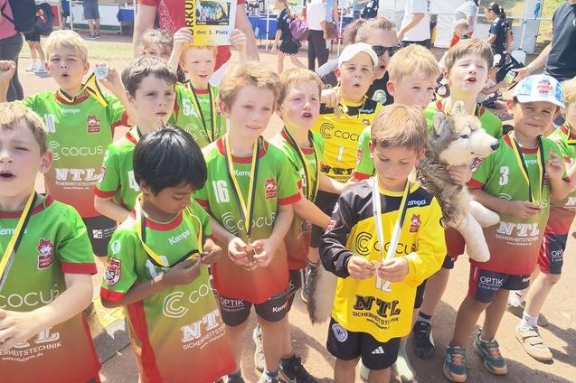 Gruppierung von Kindern in Sporttrikots mit Medaillen, versammelt auf einer Veranstaltung im Freien.