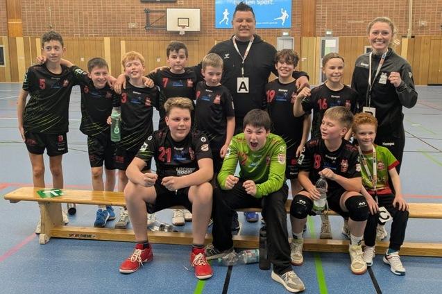 Gruppe von Kindern in Sportkleidung, die auf einer Holzbank sitzen, umgeben von Trainer in einer Sporthalle.