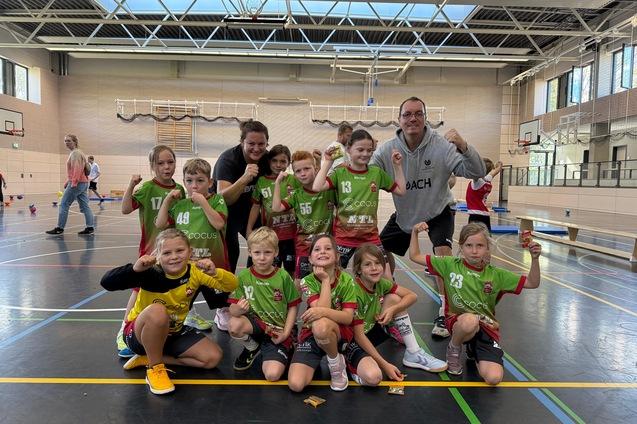 Gruppe von Kindern in Sportkleidung mit einem Trainer, posierend in einer Turnhalle.