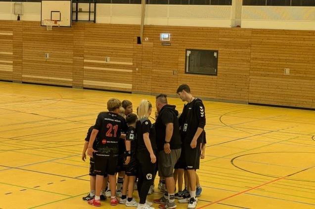 Gruppe von sieben Basketballspielern in schwarzer Kleidung versammelt sich in einer Sporthalle vor einem Spiel.