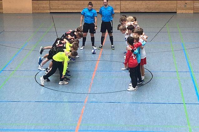 Zwei Trainer stehen zwischen zwei Gruppen von Kindern, die sich in einer Sporthalle auf eine &Uuml;bung vorbereiten.