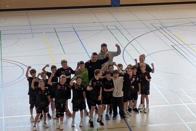 Gruppe von jugendlichen Basketballspielern in Sportkleidung, die stolz mit erhobenen Armen in einer Turnhalle posieren.