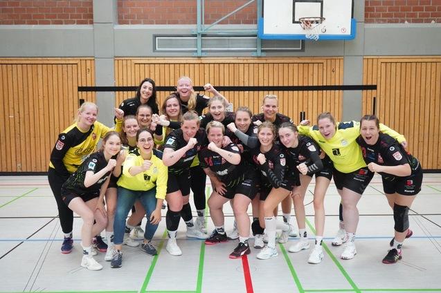 Gruppenbild von 16 Handballspielerinnen in Sportkleidung, l&auml;cheln und posieren in einer Sporthalle.