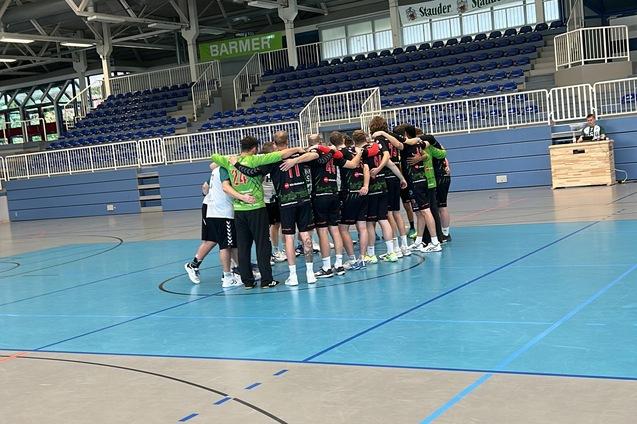 Gruppenumarmung eines Handballteams in sportlicher Kleidung auf einem blauen Hallenboden.