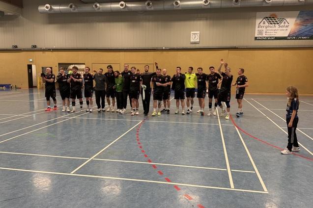 Mannschaftsaufstellung von Spielern in schwarz-wei&szlig;en Trikots in einer Halle, mit einem Kind rechts im Bild.