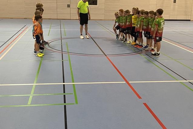Jugendliche Fu&szlig;ballspieler stehen sich auf einem blauen Hallenboden gegen&uuml;ber, ein Schiedsrichter erkl&auml;rt die Regeln.