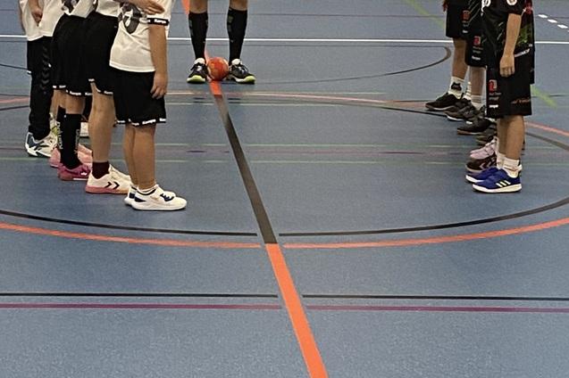 Zwei Handballmannschaften stehen sich auf dem Spielfeld gegen&uuml;ber, w&auml;hrend ein Schiedsrichter Anweisungen gibt.
