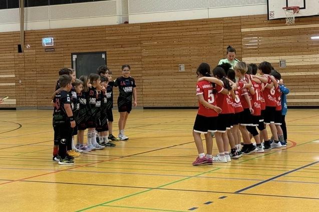 Zwei Gruppen junger Sportsler in Sportkleidung stehen sich in einer Halle gegen&uuml;ber, bereit f&uuml;r das Spiel.