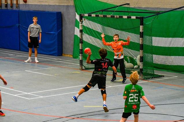 Zwei Handballspieler im Spiel: Einer wirft auf das Tor, der Torwart bereitet sich auf den Schuss vor.