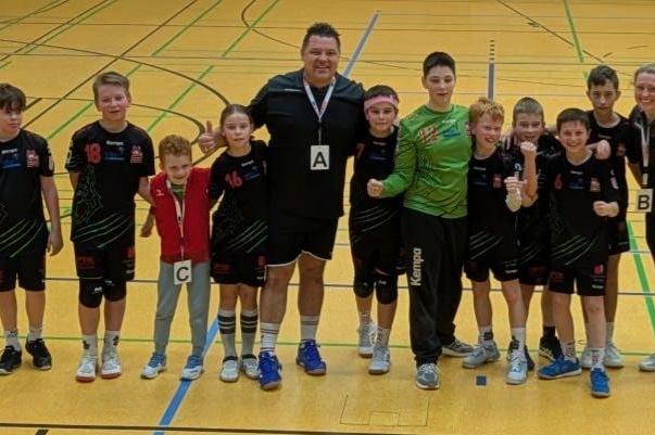 Gruppe von zehn jungen Sportlern und einem Trainer in Sportkleidung, l&auml;chelnd in einer Sporthalle, bereit f&uuml;r ein Spiel.