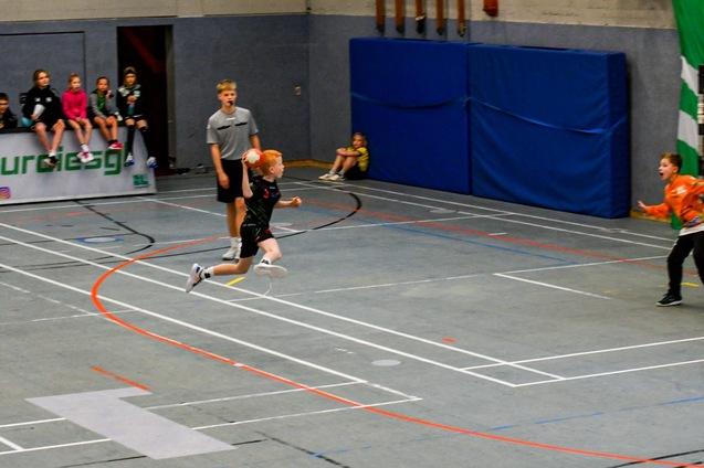 Ein junger Handballspieler springt zum Tor, w&auml;hrend der Torwart sich vorbereitet, im Hintergrund Zuschauer.