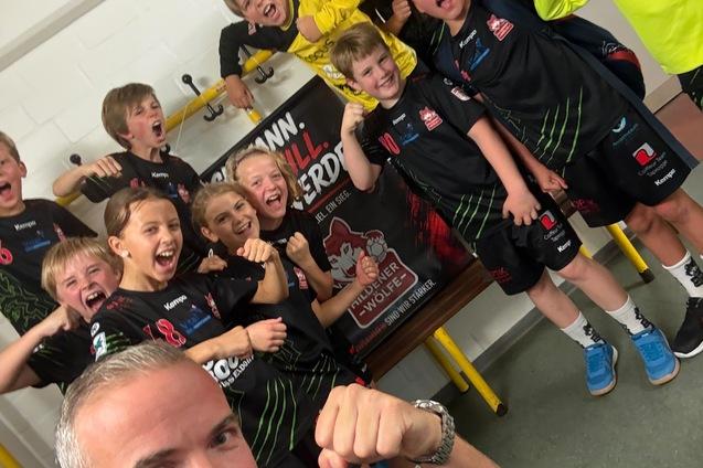 Gruppe jubelnder Kinder in Sportkleidung mit Trainer, posieren fr&ouml;hlich in einem Umkleideraum.