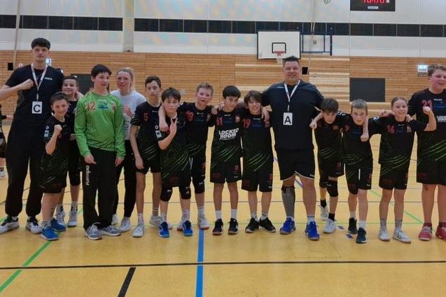 Gruppe von Jugendlichen in Sportkleidung, umgeben von Trainern, posiert auf einem Basketballfeld mit Medaillen.