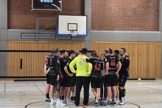 Handballmannschaft steht im Kreis, w&auml;hrend der Trainer Anweisungen gibt, mit Spielstand von 34 zu 42 auf der Anzeigetafel.