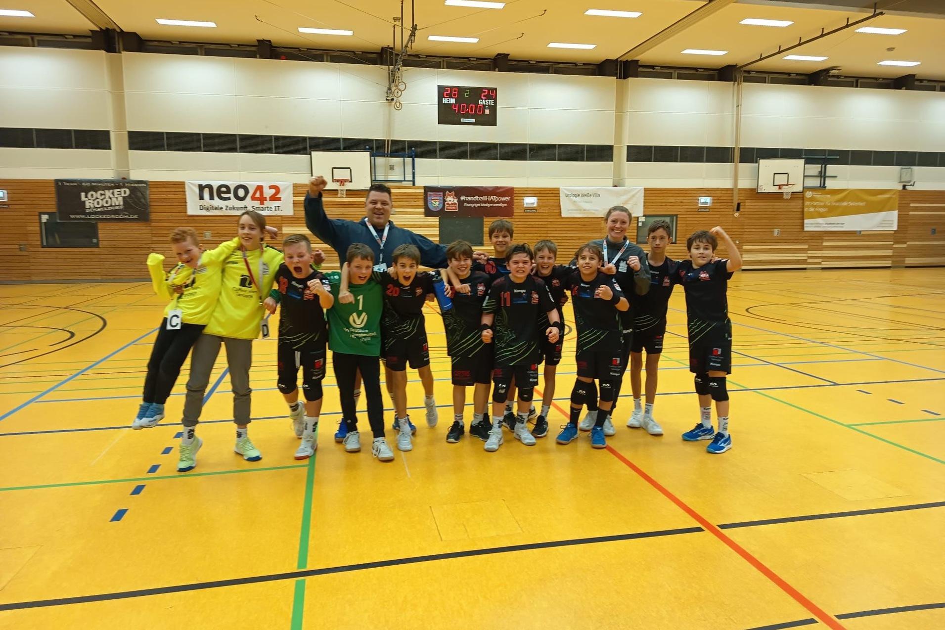 Gruppe von Kindern in Sportkleidung, lächeln und zeigen Medaillen in einer Turnhalle mit Basketballkörben im Hintergrund.