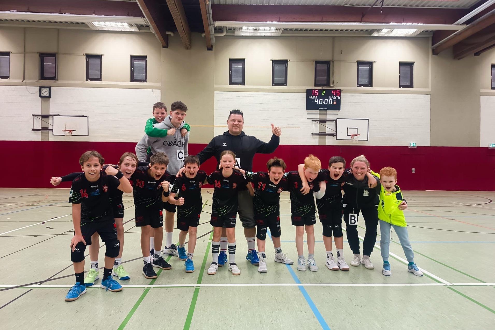 Gruppe von Kindern in Sportkleidung mit Trainer in einer Sporthalle, alle jubeln zusammen nach einem Spiel.