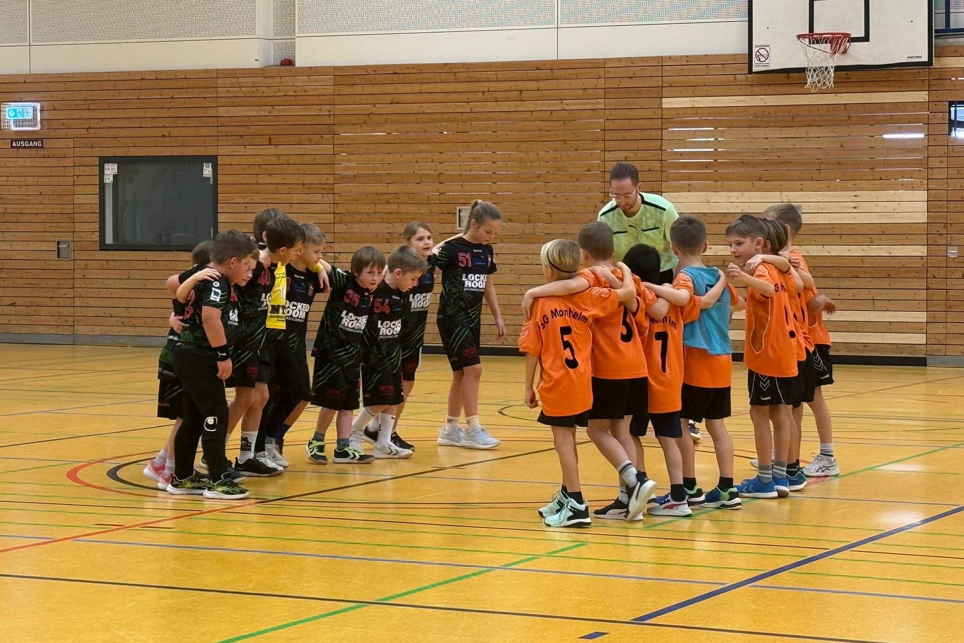 Zwei Gruppen von Kindern in Sportkleidung stehen sich auf einem Handballfeld gegenüber und umarmen sich.