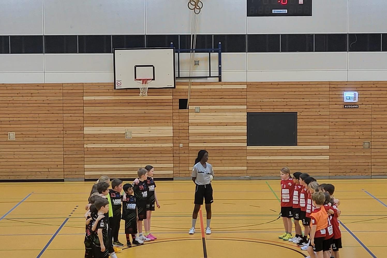 Zwei Gruppen von Kindern in Sportkleidung stehen sich auf einem Handballfeld gegenüber, wartend auf den Spielbeginn.