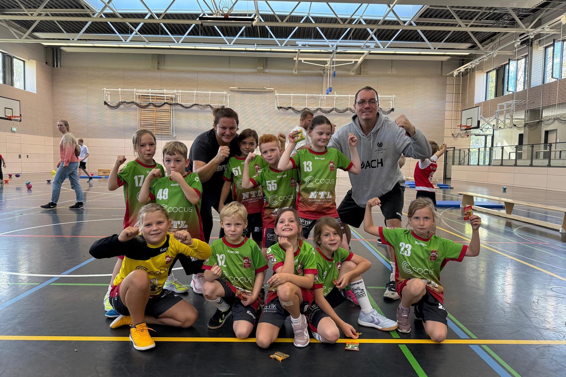 Gruppe von Kindern in Sportkleidung mit einem Trainer, posierend in einer Turnhalle.