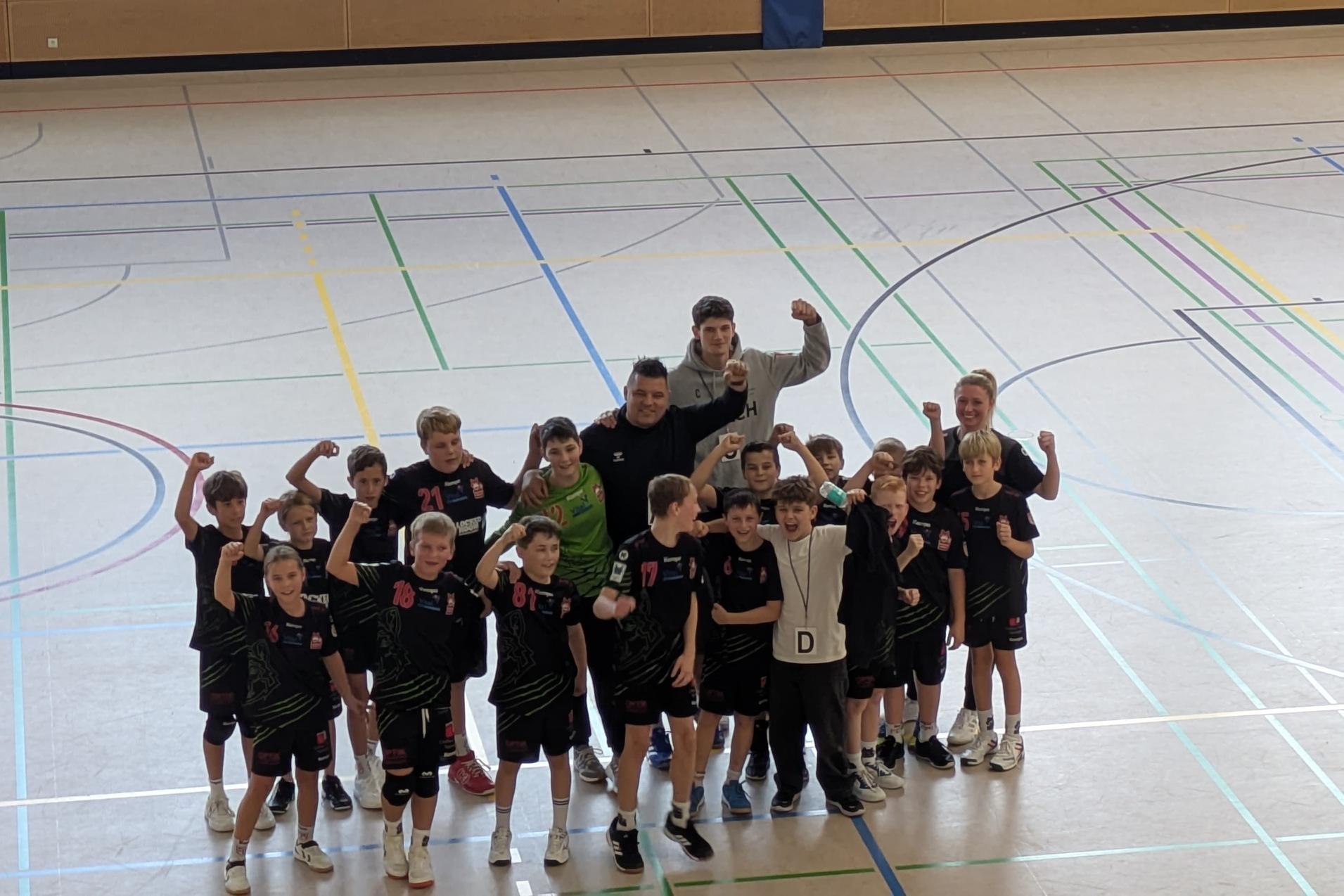 Gruppe von jugendlichen Basketballspielern in Sportkleidung, die stolz mit erhobenen Armen in einer Turnhalle posieren.