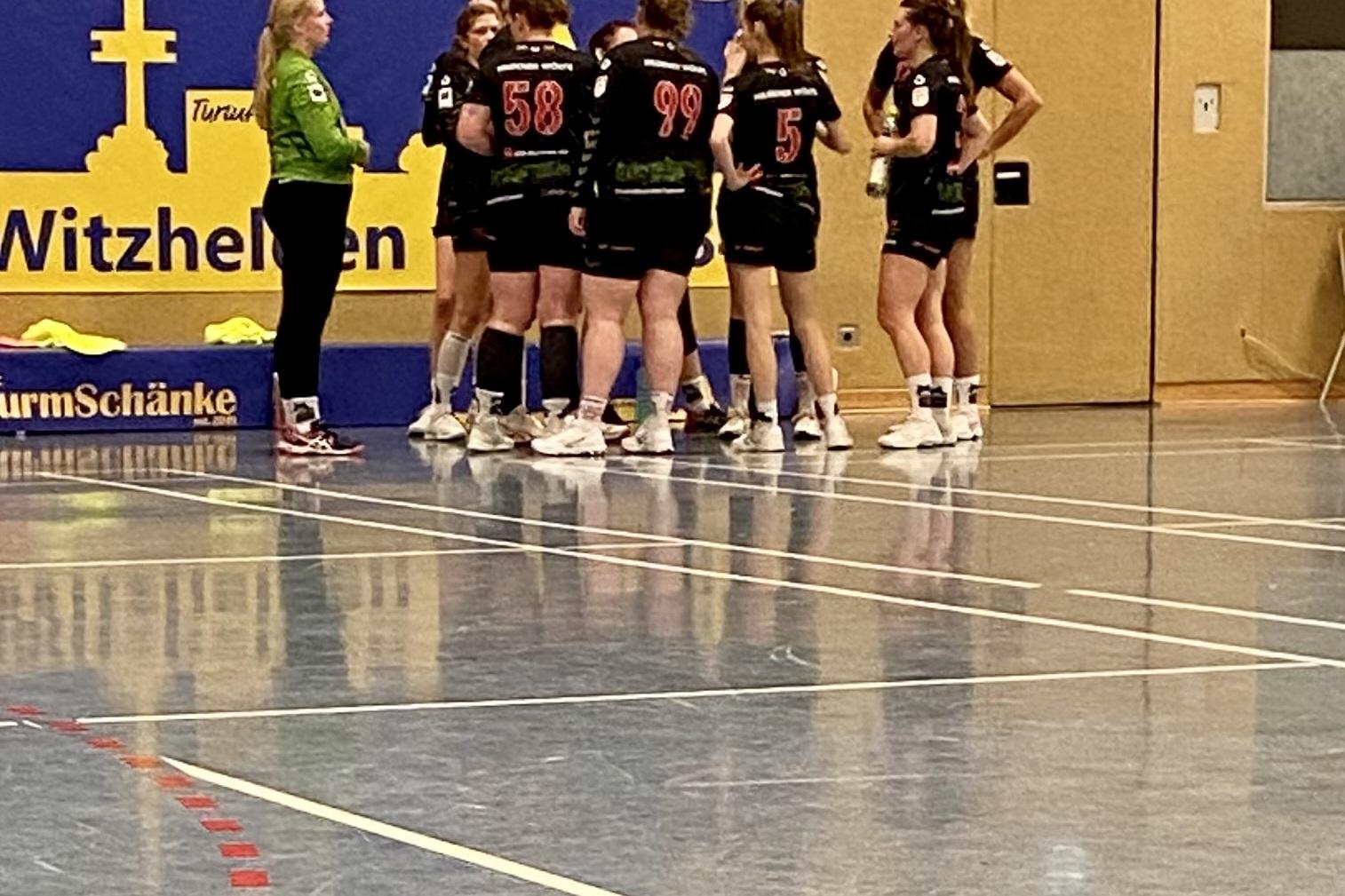 Gruppenansprache eines Handballteams in einer Sporthalle mit blauem Banner im Hintergrund.