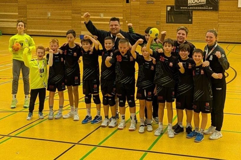 Gruppe jubelnder Kinder, Trainer und Betreuer in Sportkleidung auf einem Handballfeld.