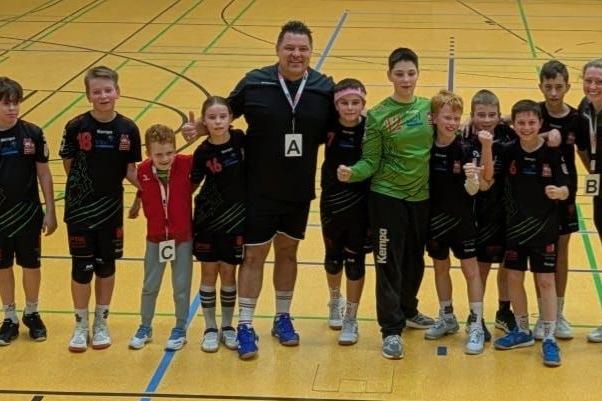 Gruppe von zehn jungen Sportlern und einem Trainer in Sportkleidung, lächelnd in einer Sporthalle, bereit für ein Spiel.