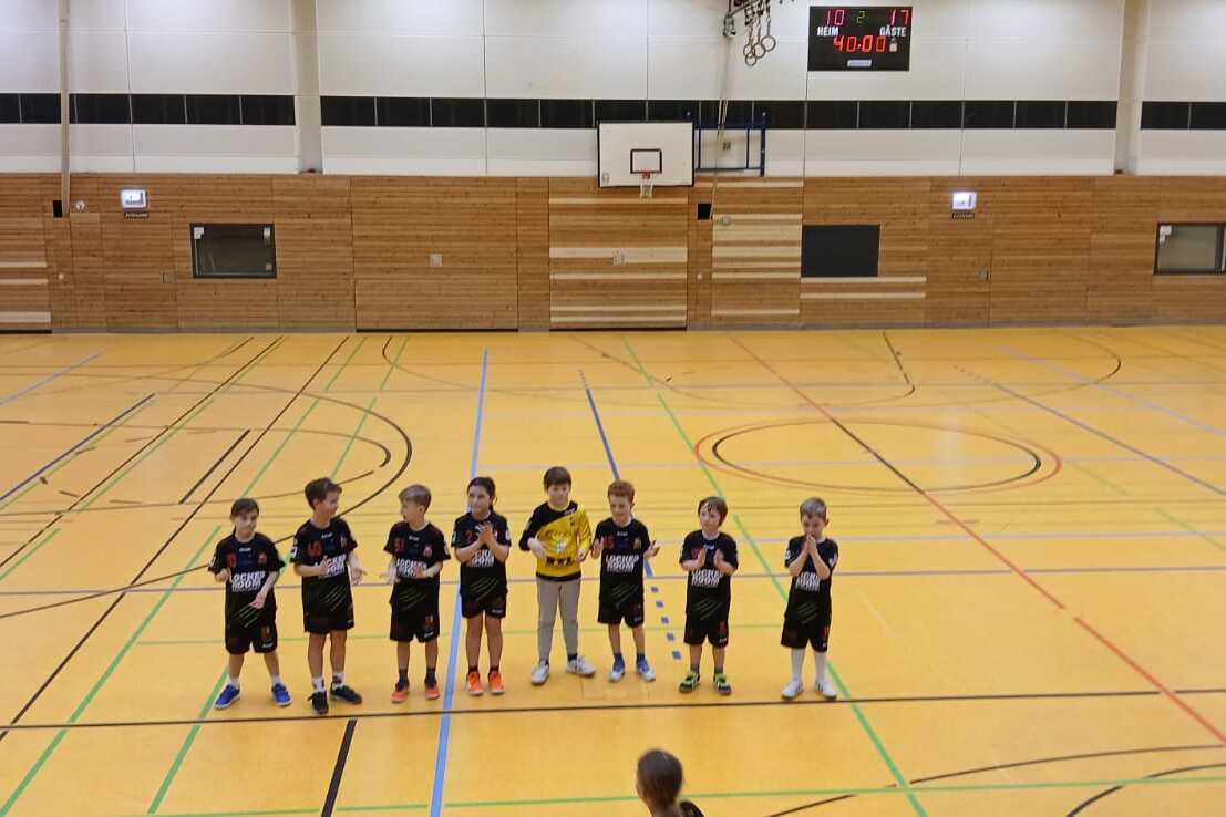 Gruppe von sieben Kindern in Sportkleidung steht auf einem Holzfußboden in einer Sporthalle.