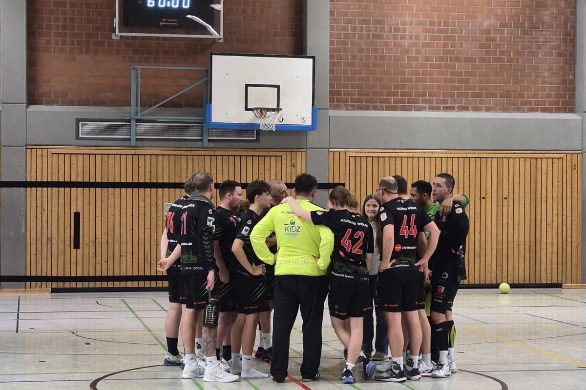 Handballmannschaft steht im Kreis, w&auml;hrend der Trainer Anweisungen gibt, mit Spielstand von 34 zu 42 auf der Anzeigetafel.