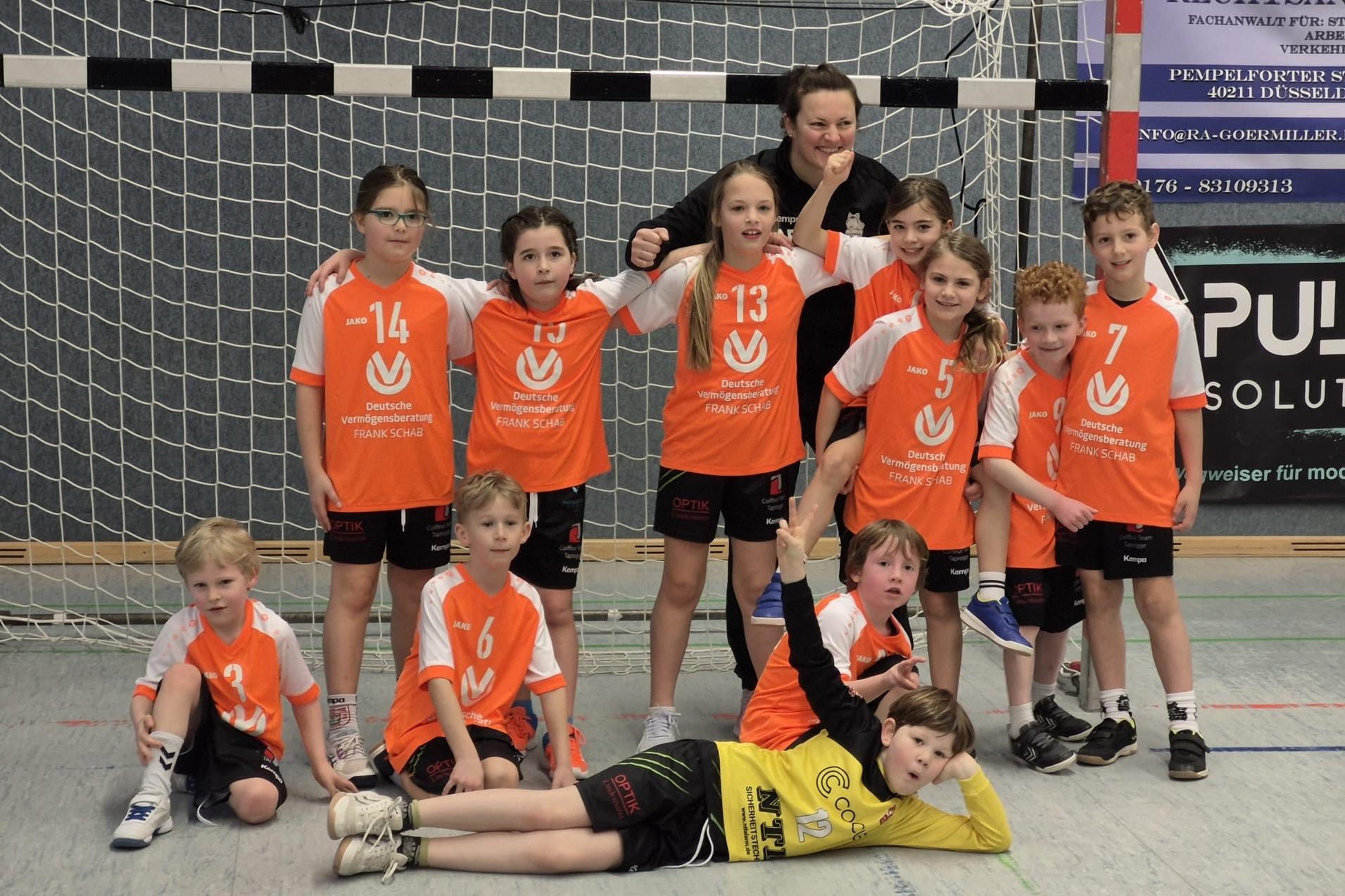Gruppenfoto einer Kinderhandballmannschaft in orangefarbener Sportbekleidung vor einem Tor.