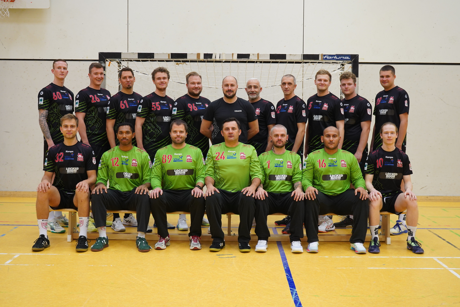 Mannschaftsfoto einer Handballmannschaft, bestehend aus 17 Spielern in schwarzen und gr&uuml;nen Trikots, vor einem Tor.