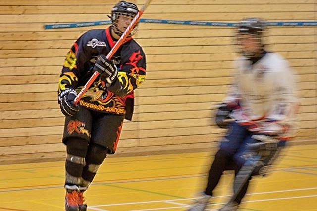Aktion im Hallen-Hockey mit einem Spieler in schwarzem Trikot und einem anderen Spieler im Hintergrund in Bewegung.