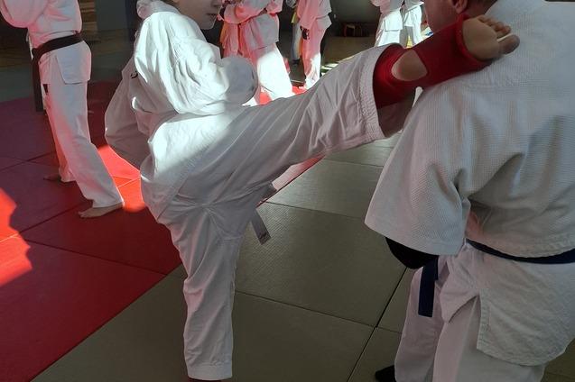 Junge Karateka f&uuml;hrt einen Kniestand mit rotem Schoner gegen einen Erwachsenen in einer Trainingshalle aus.