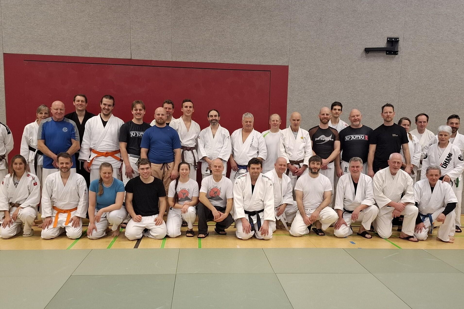Gruppenfoto von Judo-Praktizierenden in weißen Anzügen auf einer Trainingsmatte, vor einer grauen Wand.