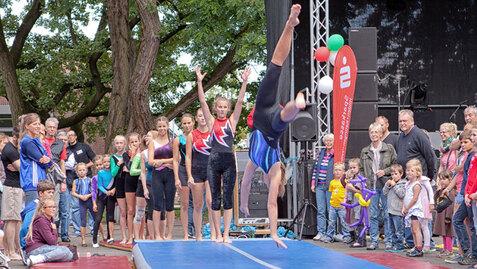 Zwei Turnerinnen f&uuml;hren eine Gymnastik&uuml;bung auf einem blauen Wettkampfsprungtisch vor einer Zuschauermenge vor.