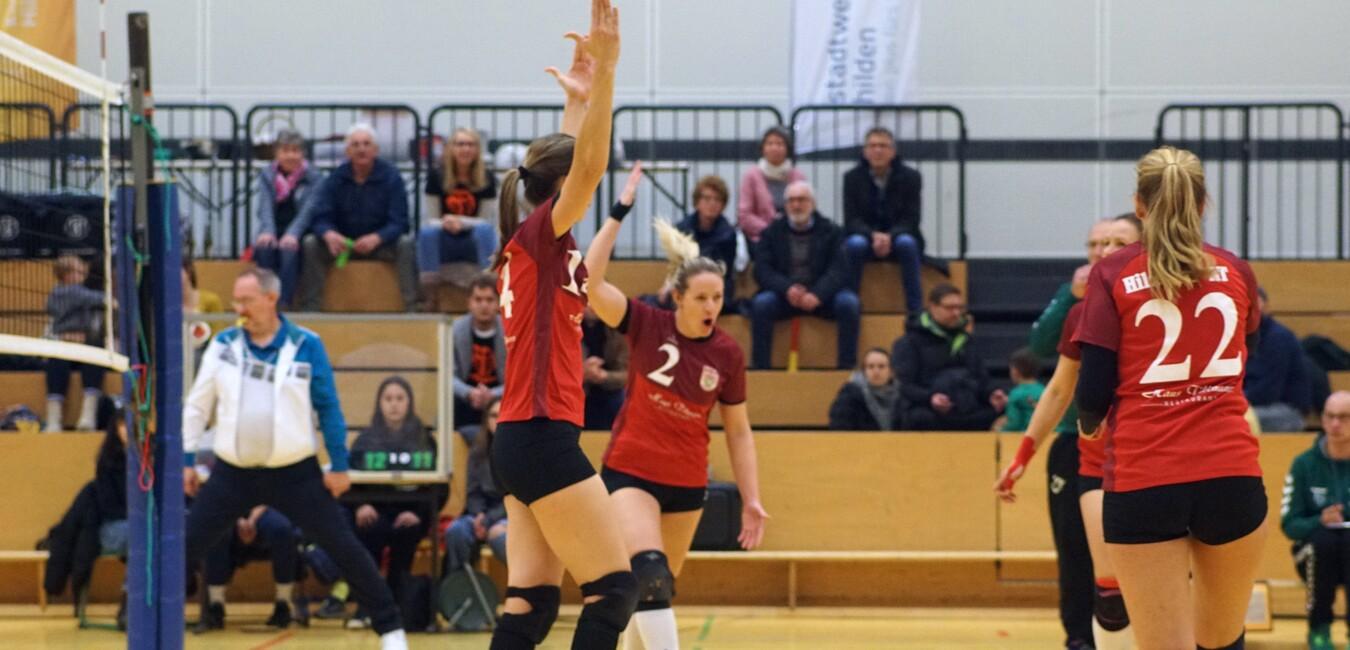 Spielszene eines Volleyballspiels mit jubelnden Spielerinnen in roten Trikots und Zuschauern im Hintergrund.