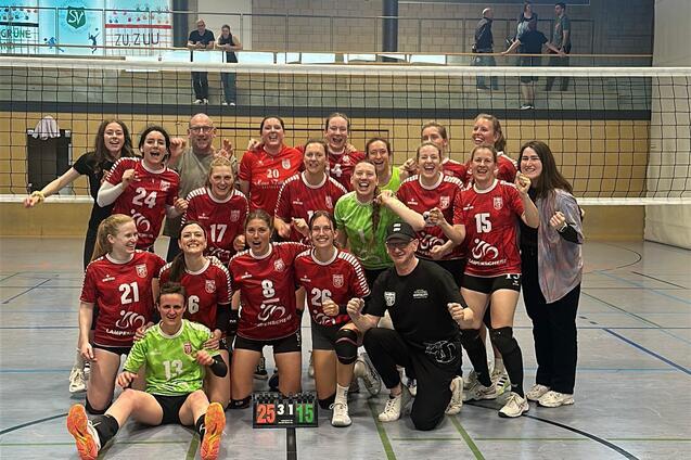 Gruppennahaufnahme von einem Volleyballteam in roten Trikots, umrahmt von Trainer und Fans, nach dem Spiel.