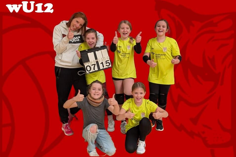 M&auml;dchenmannschaft U12 posiert mit Trainerin vor Spielstandsanzeiger auf rotem Hintergrund, alle zeigen Daumen hoch.